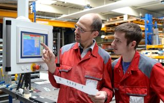 Lavoratore adulto che insegna a usare una macchina a un collega più giovane in ambiente industriale