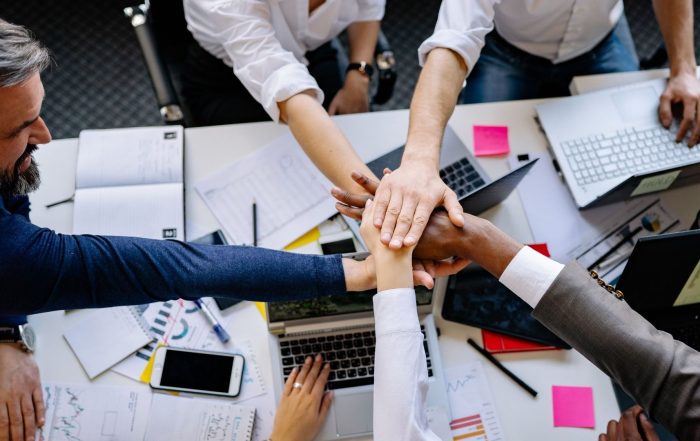 Un gruppo di professionisti che mette le mani insieme al centro di un tavolo da lavoro, a simboleggiare il successo del team e la cooperazione aziendale.