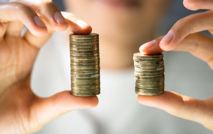 Close-up di due mani che tengono due pile di monete di altezza diversa, simbolo di disparità salariale e disuguaglianza economica.