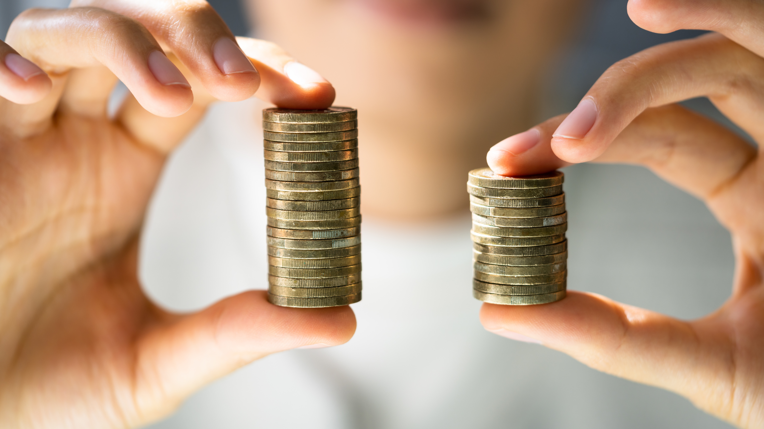 Close-up di due mani che tengono due pile di monete di altezza diversa, simbolo di disparità salariale e disuguaglianza economica.